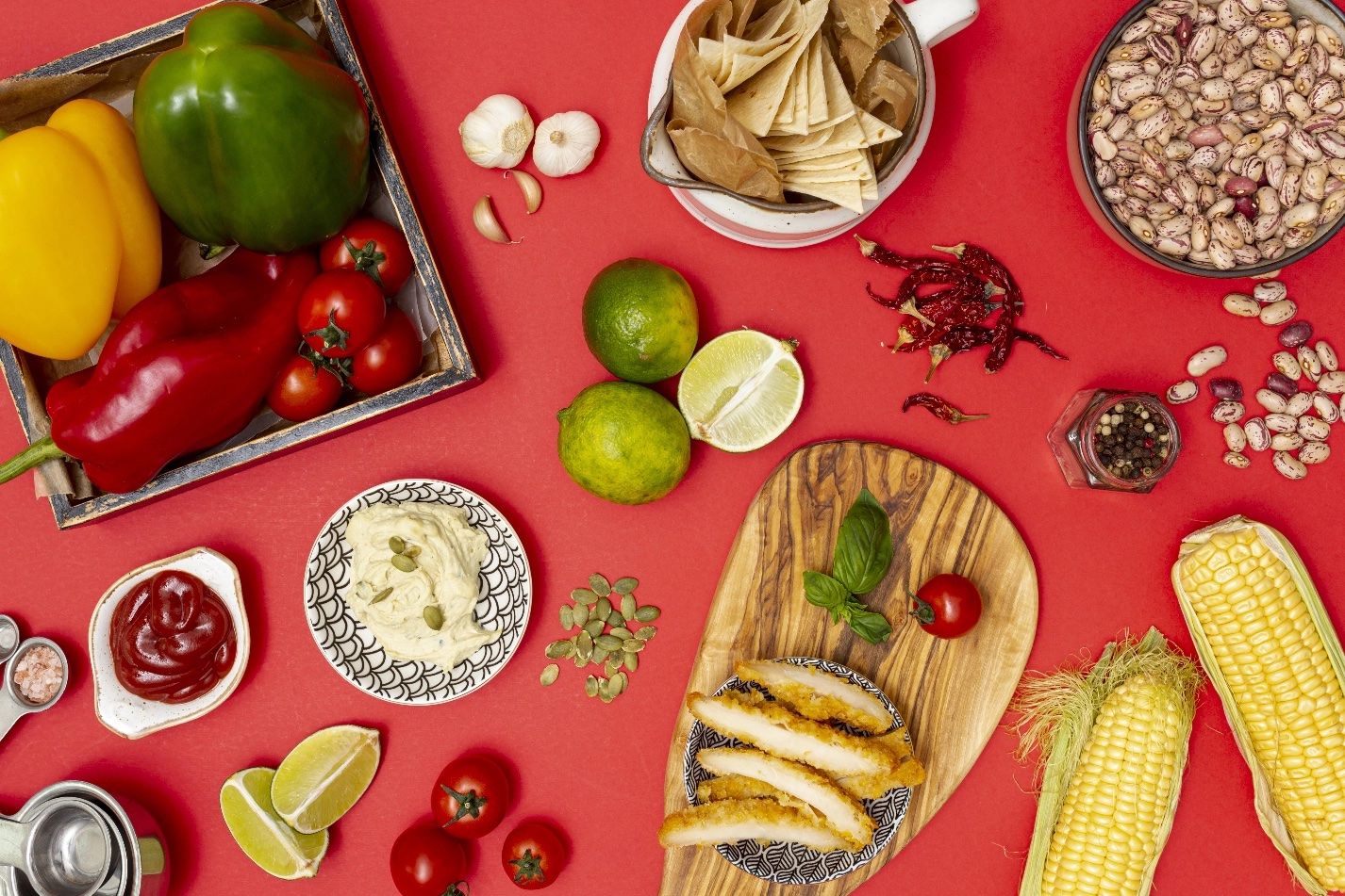 Table rouge garnie de poivrons, citrons verts, maïs, nachos et sauces
