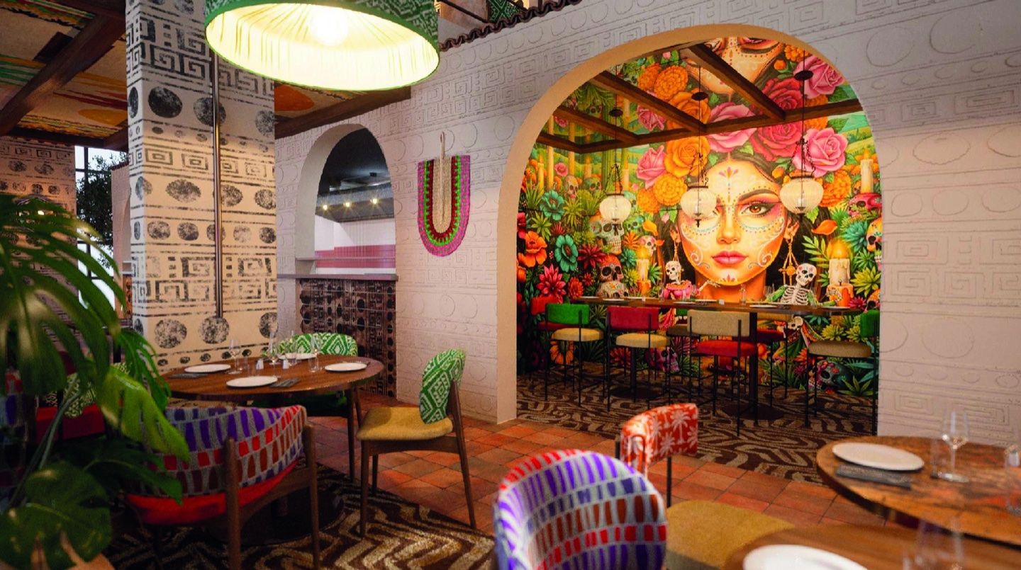 Salle de La Cantina : fresque colorée d’un visage fleuri sous une arche, tables dressées