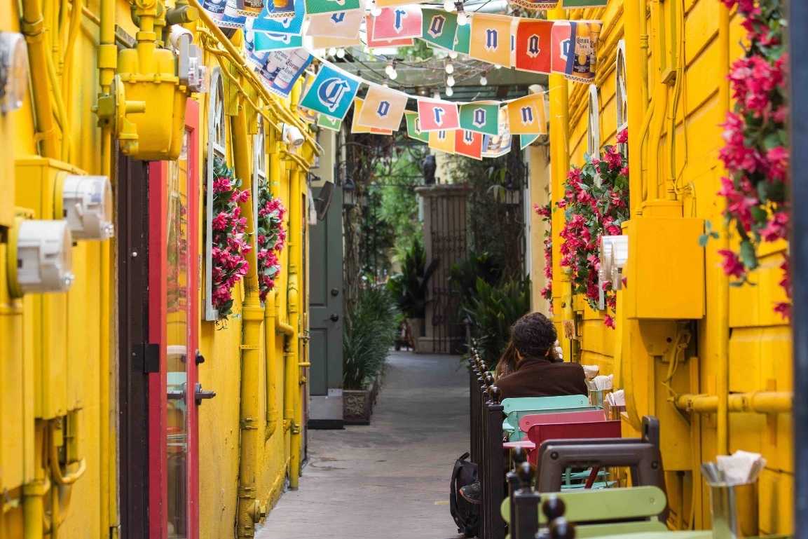 Ruelle aux façades jaunes, fleurs et guirlandes de fanions, une table en terrasse